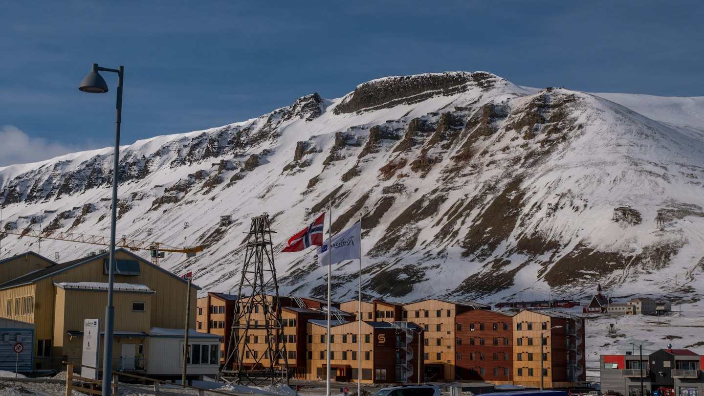 Moderne bygninger og industrikraner ligger under et snødekt fjell.