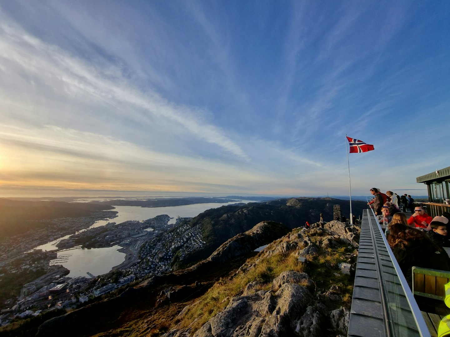 Fotturister står på en steinete fjelltopp med utsikt over en fjord.