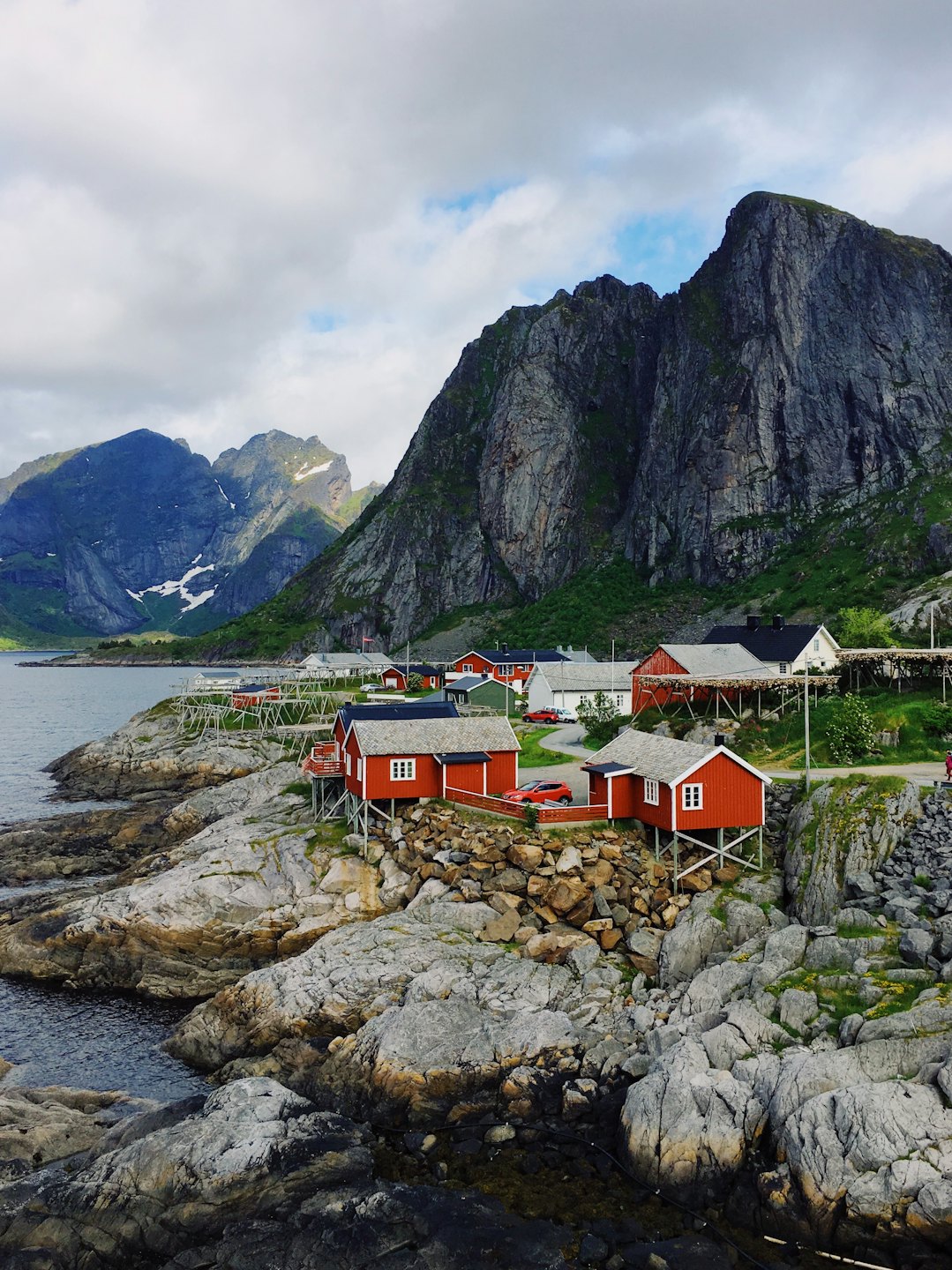 Røde trehus på påler langs en steinete kystlinje.